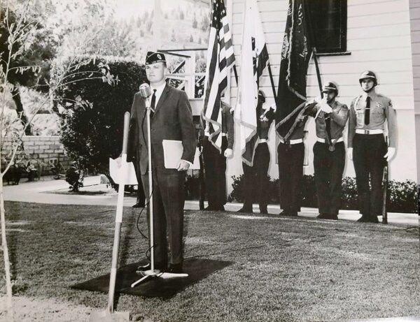 vintage image of Vetter in unifom stading infront of soldier color guard holding flags.