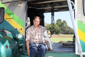 Hiker and his dog are sitting in the door of the Heliocoptor. 