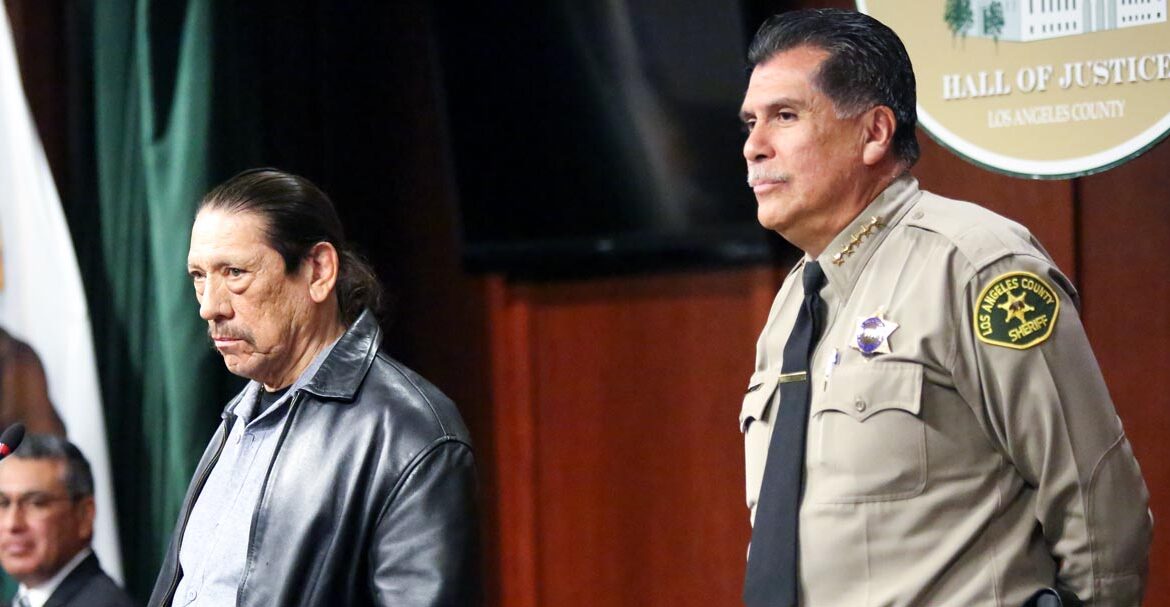 Actor Danny Trejo is standing at a podium with Sheriff Luna Standing near by.