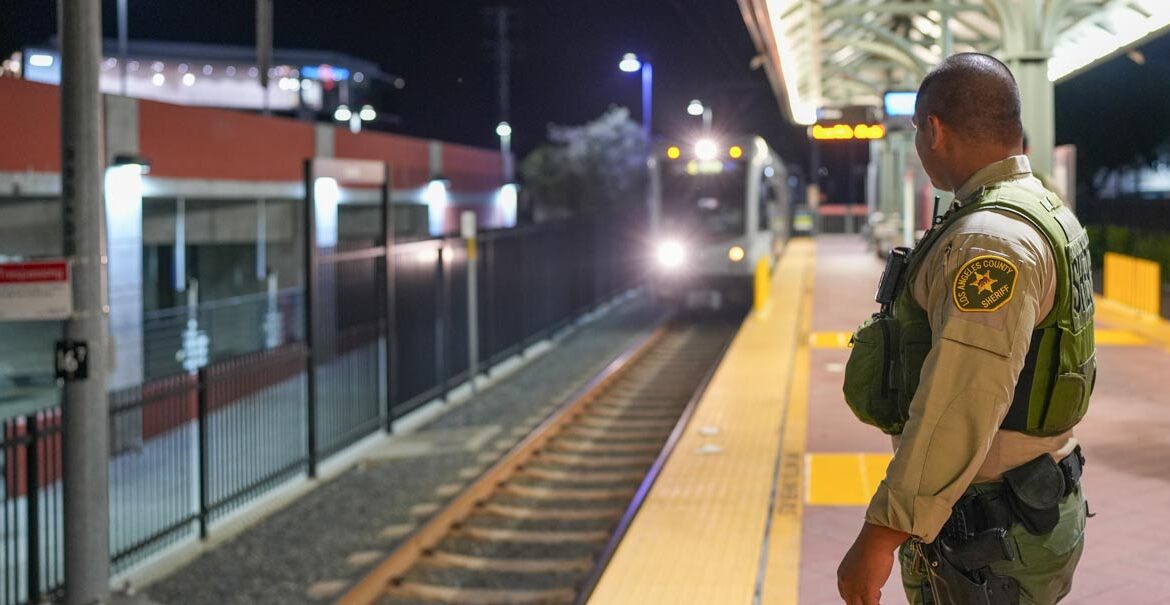 Deputy Sheriff is standing at the edge of a platform waiting for a train to arrive, he train is heading in to the station with the front headlight visible in the darkness.