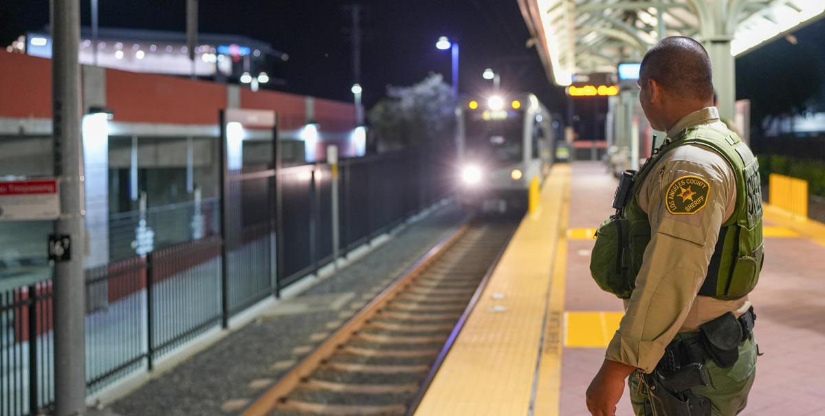 Deputy Sheriff is standing at the edge of a platform waiting for a train to arrive, he train is heading in to the station with the front headlight visible in the darkness.