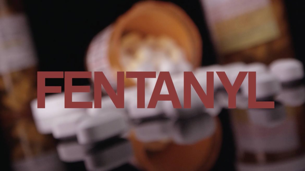 image of an overturned pill bottle with pill spilling onto a black reflective table top. The word Fentanyl is displayed in a maroon font.