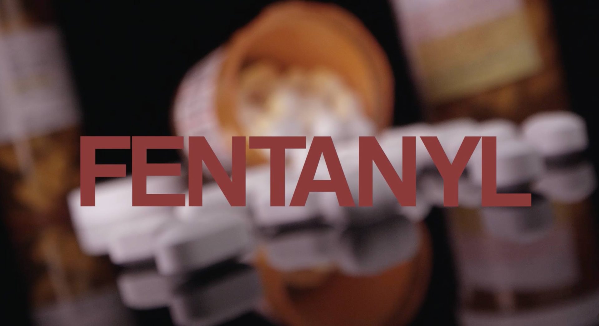 image of an overturned pill bottle with pill spilling onto a black reflective table top. The word Fentanyl is displayed in a maroon font.