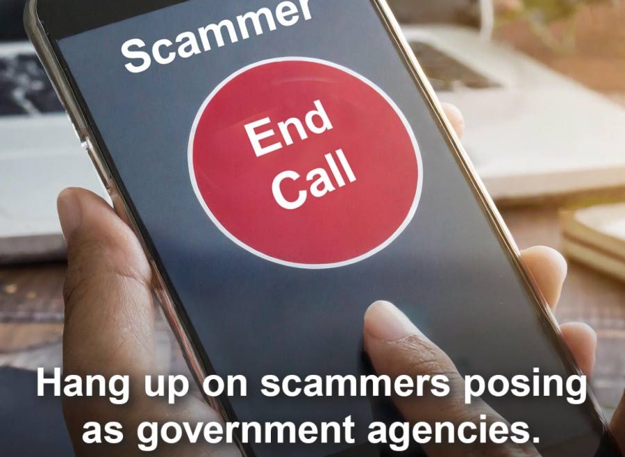 A hand holding a cell phone; on the screen, the caller ID says "Scammer" with a large red "End Call" button below