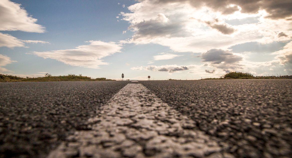 Image of center line on a road. Sky is blue with clouds.