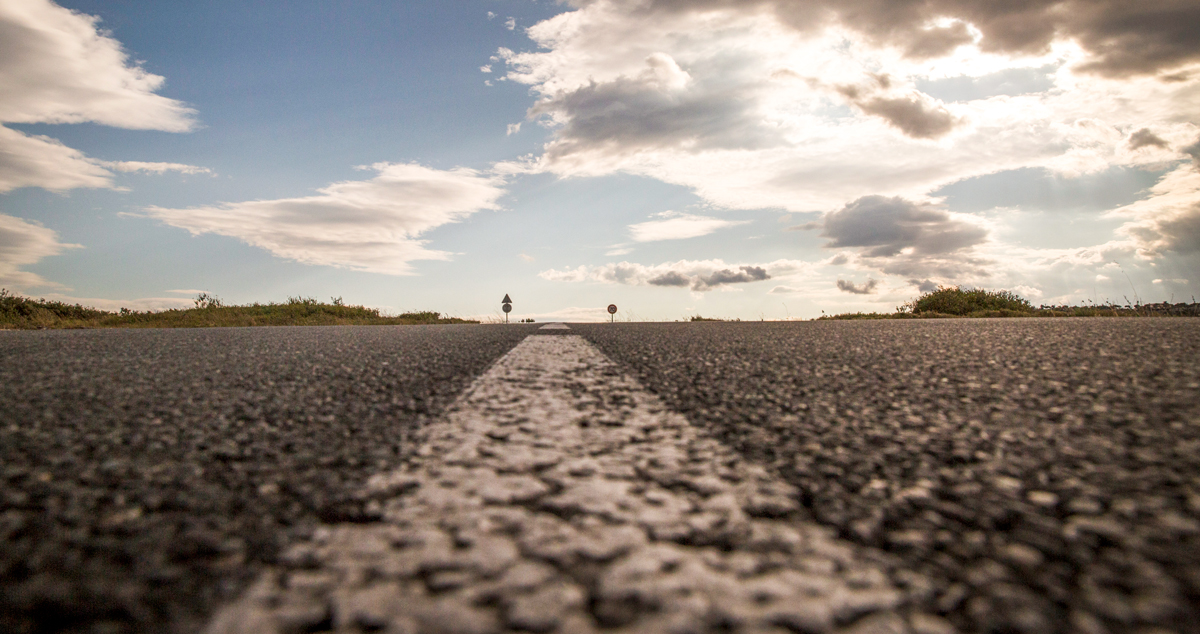 Image of center line on a road. Sky is blue with clouds.