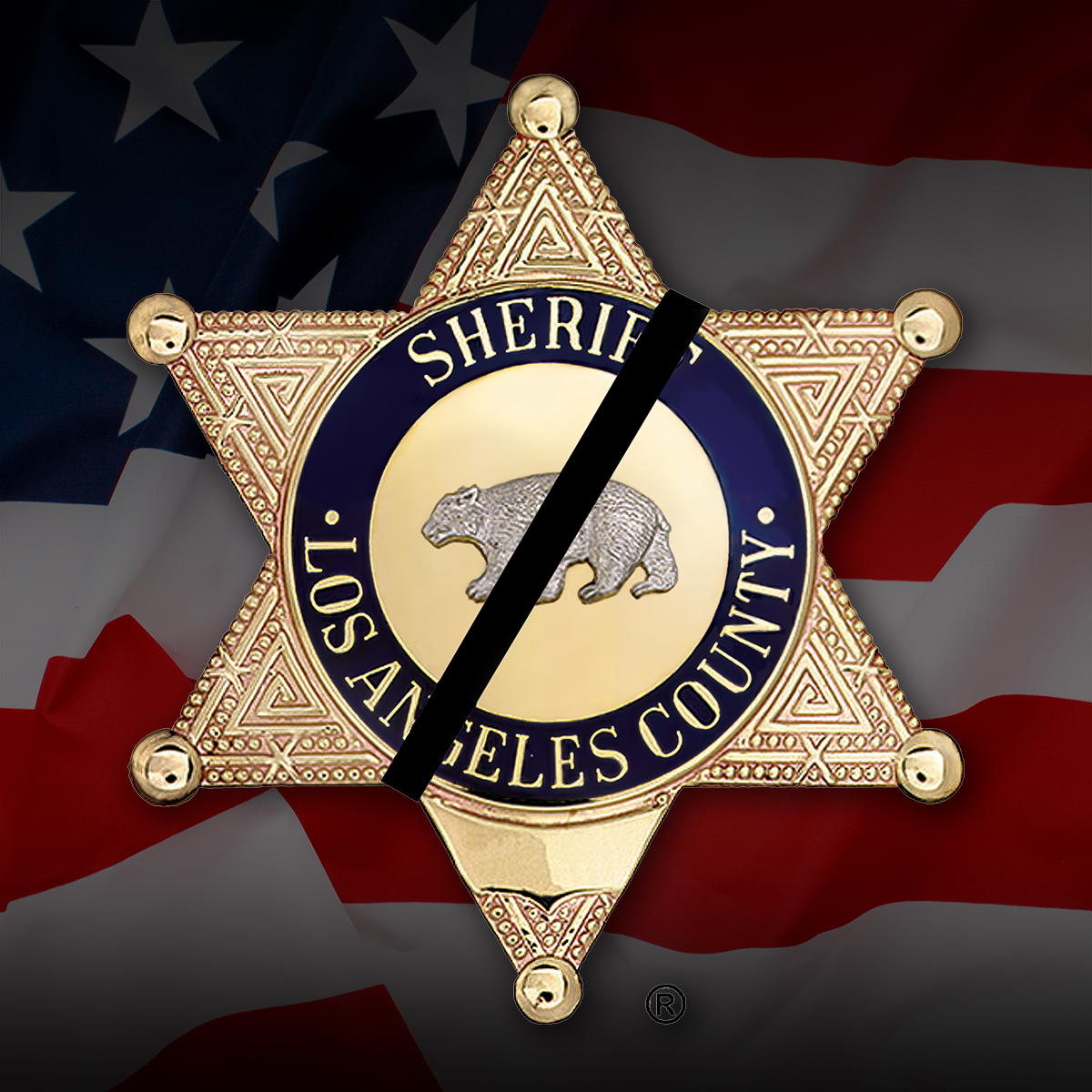 Los Angeles County Sheriff's Badge, Gold, six point badge. Sheriff, Los Angeles County is written in the center blue line of the badge, and a bear engraving is in the center, the bear is on all fours and walking left. There is a black band on the badge going right to left, diagnally, The badge sits on an image of the american flag.